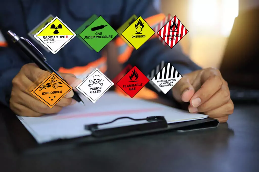 Security officers hold clipboards and inspect the storage of dan A person is writing on a clipboard emblazoned with hazard symbols like radioactive, gas under pressure, and more. The background is blurred, but the importance of HAZPlus Safety Training shines through amidst the explosive imagery of poison and flammable gas warnings.