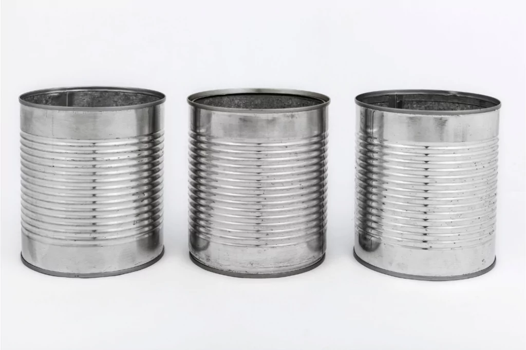 Three empty, silver tin cans with ridged surfaces are aligned side by side against a plain white background.