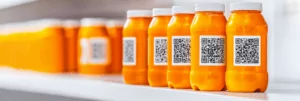 AdobeStock_1008327523 Row of orange bottles with QR codes on a white shelf, with some bottles blurred in the background.