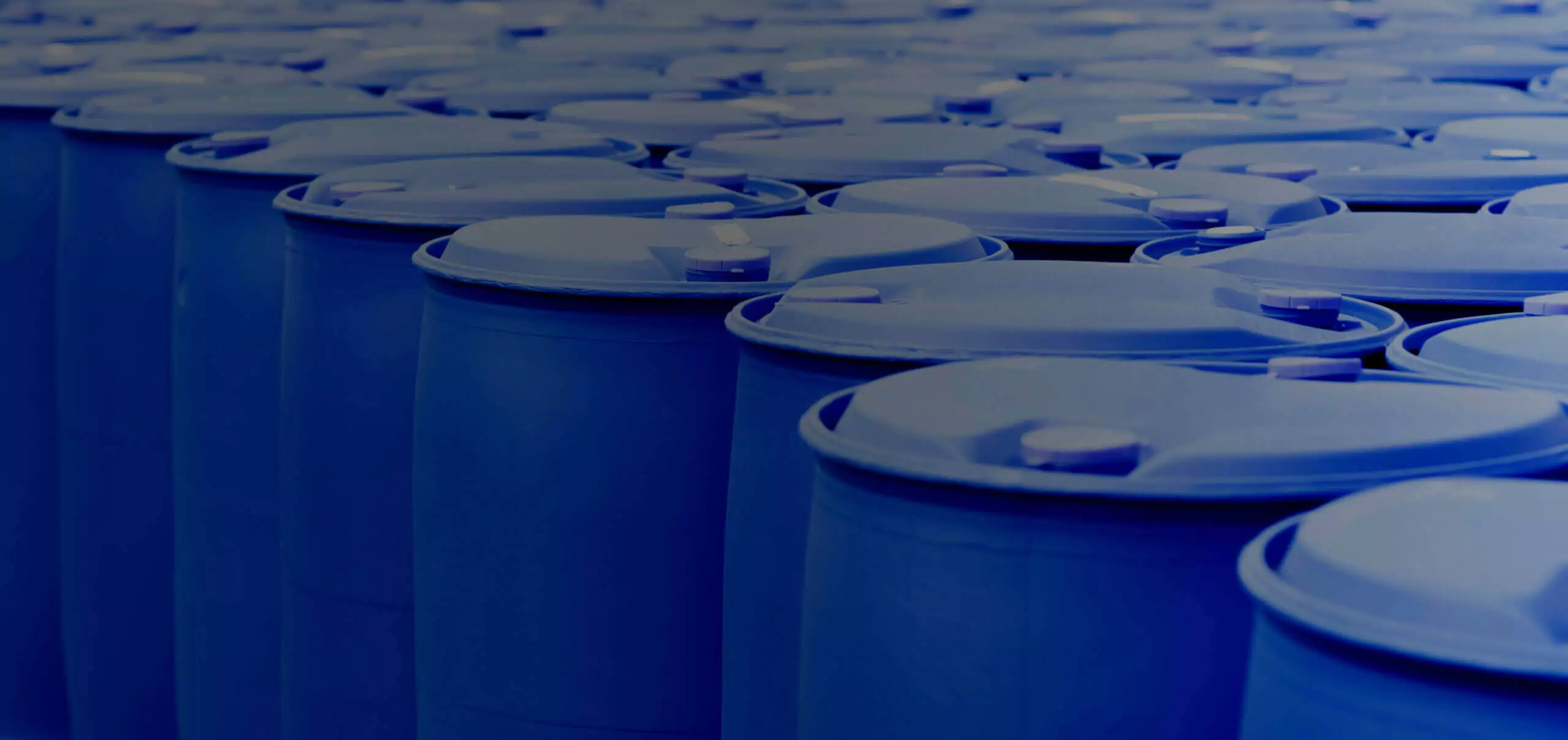 A large group of blue plastic barrels arranged in rows. The barrels have round lids and are tightly packed together, filling the entire frame. The image is tinted in a blue hue.