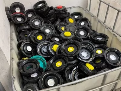 A large container filled with numerous black plastic reels, each with colorful centers in red, yellow, green, or white. The container is situated against a plain wall in an industrial setting.